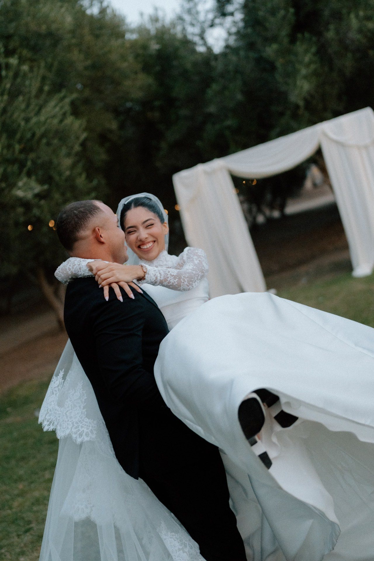 Groom carrying a smiling bride outdoors.