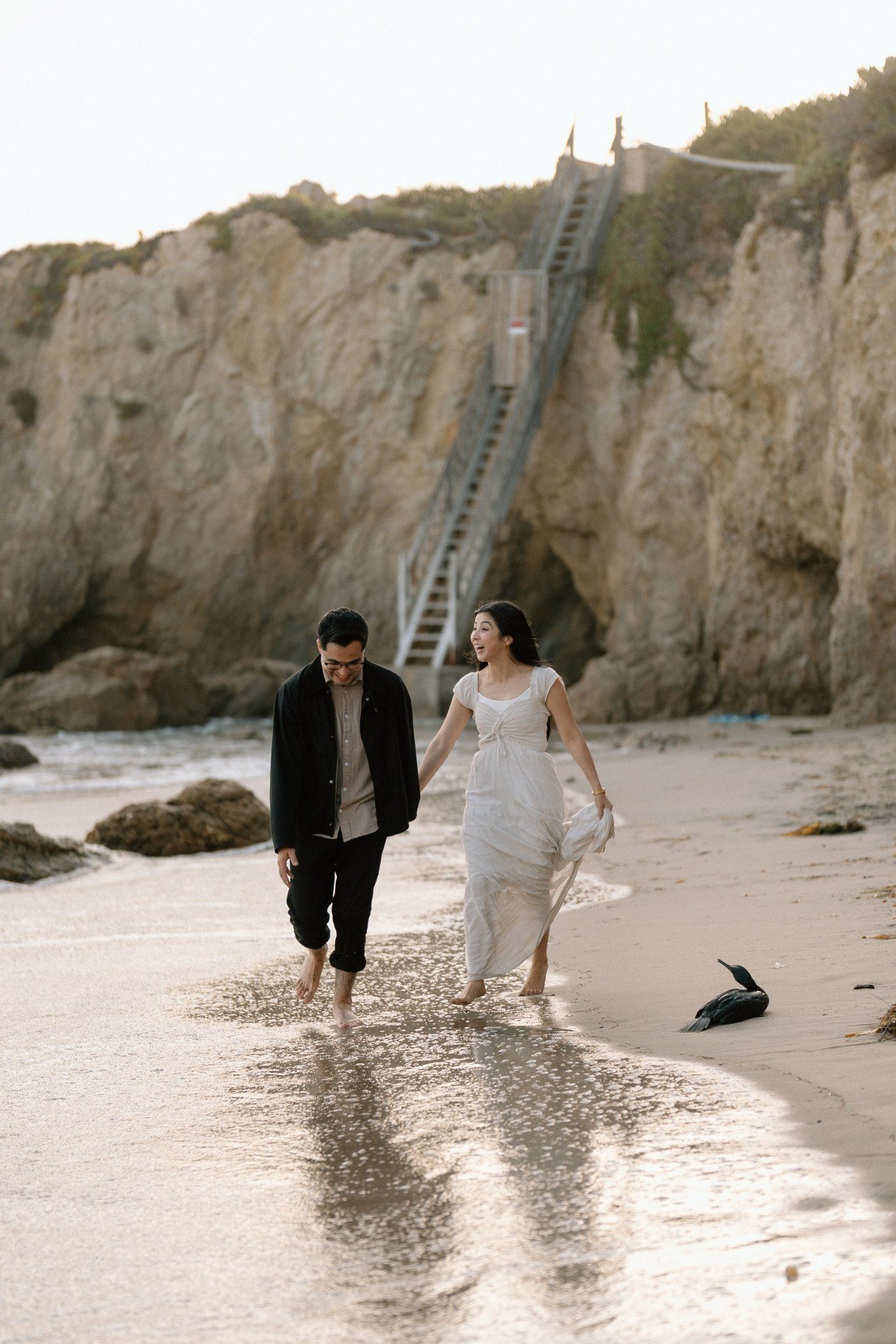 Couple walking barefoot beside the water and coastal cliffs.