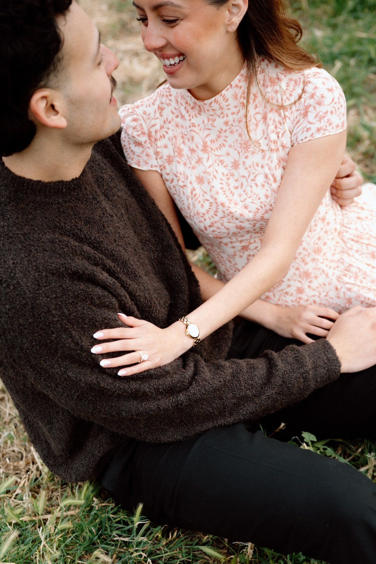 Couple smiling together while seated on the grass.