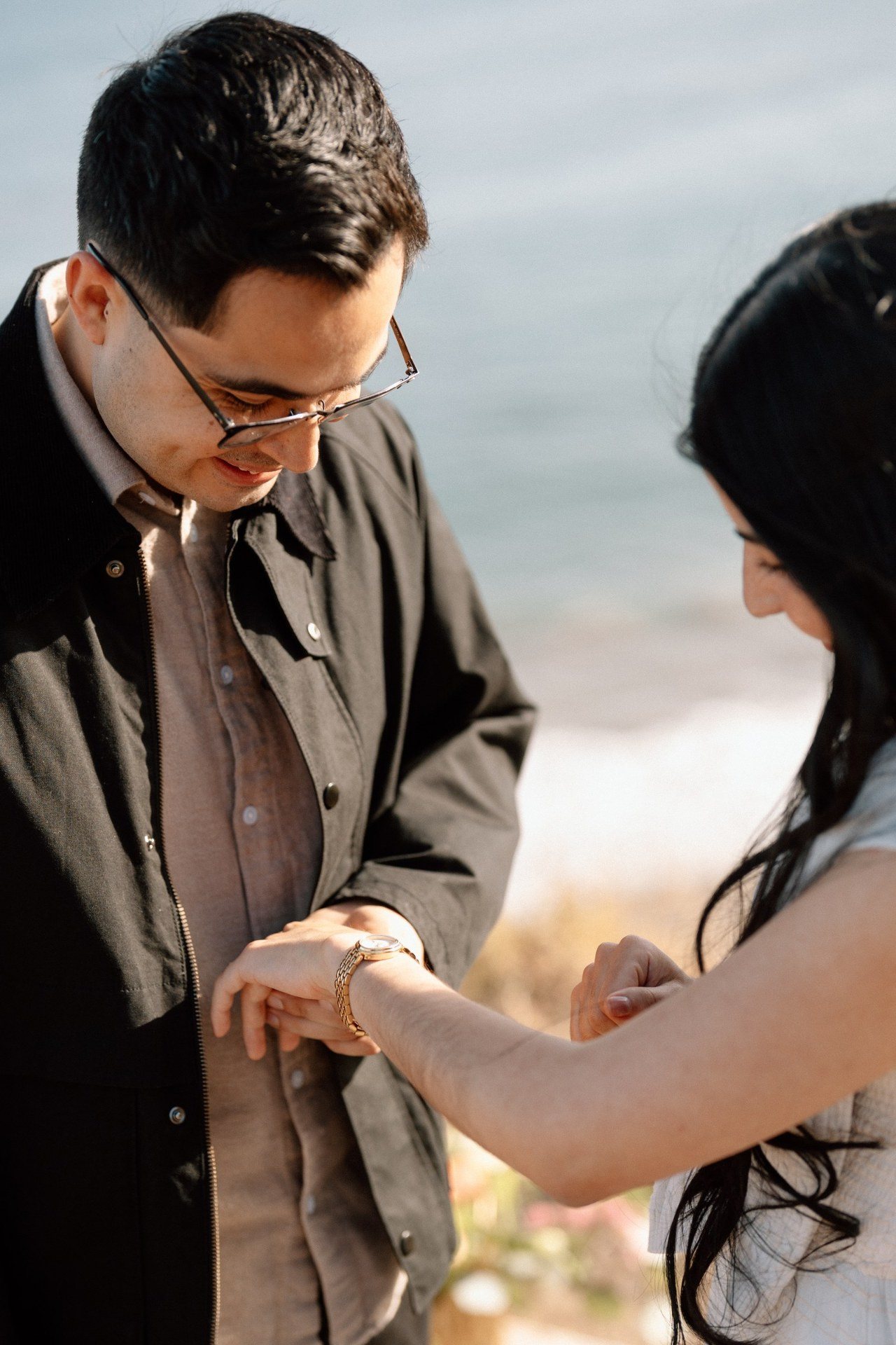 Close-up of a couple admiring an engagement ring beside the ocean.