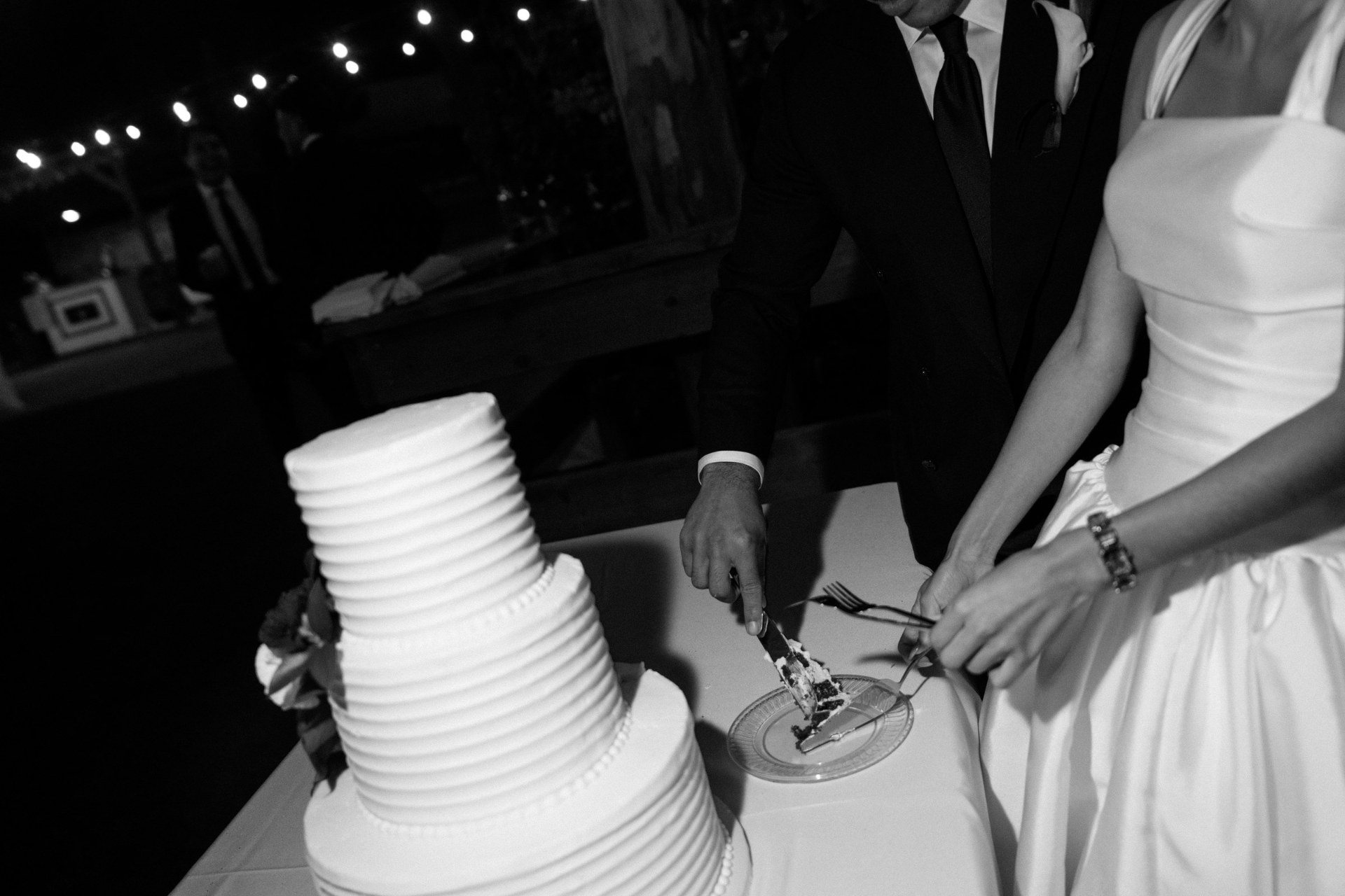 Black-and-white close-up of newlyweds cutting their wedding cake.
