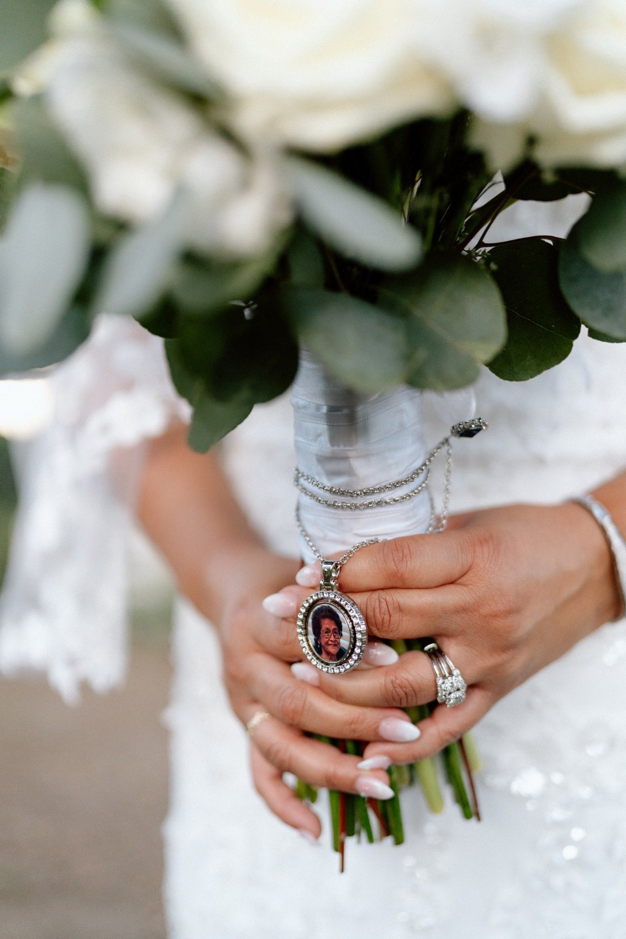 Close-up of a white bridal bouquet, rings and a keepsake charm.
