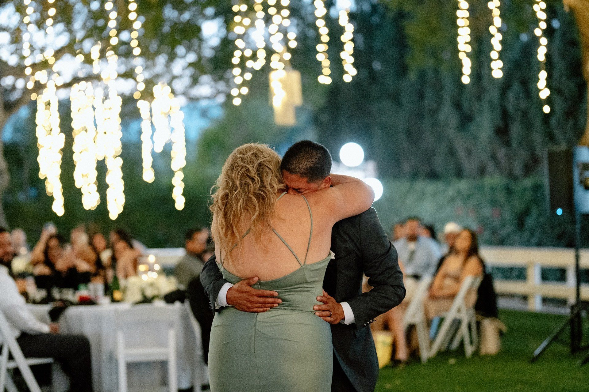 A warm embrace on the reception dance floor beneath string lights.